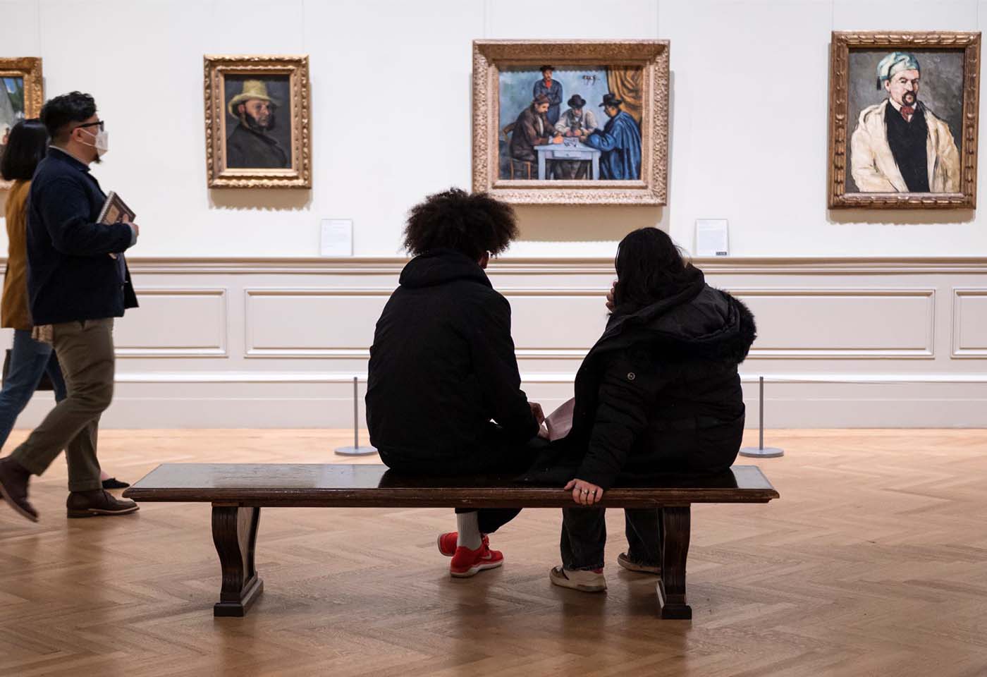 Two visitors sit on a bench in The Met's European Paintings galleries with their backs towards us.